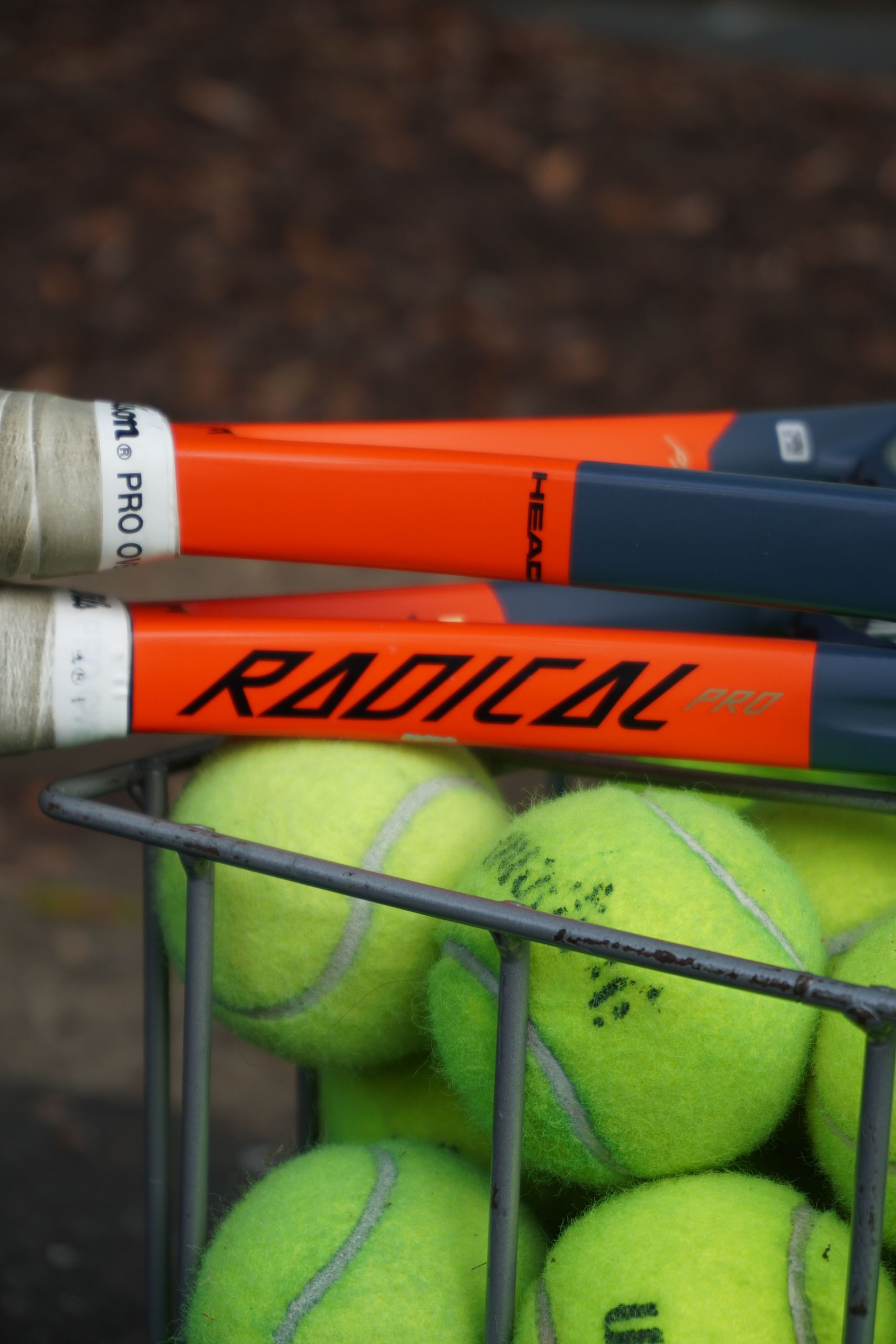 Close-up of tennis rackets and balls in a basket outdoors, showcasing sports equipment details.