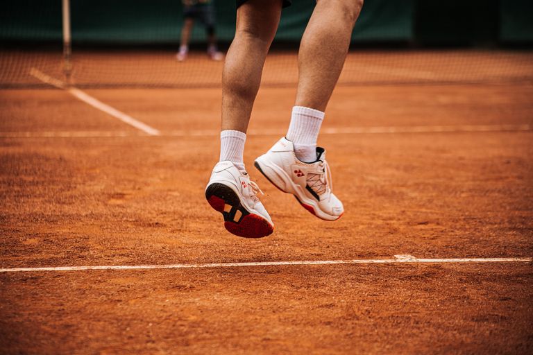 Low angle view of a tennis player jumping on a clay court, showcasing movement.