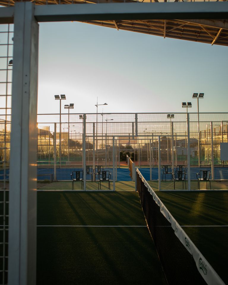 Peaceful sunset over empty tennis courts surrounded by fences and sports equipment.